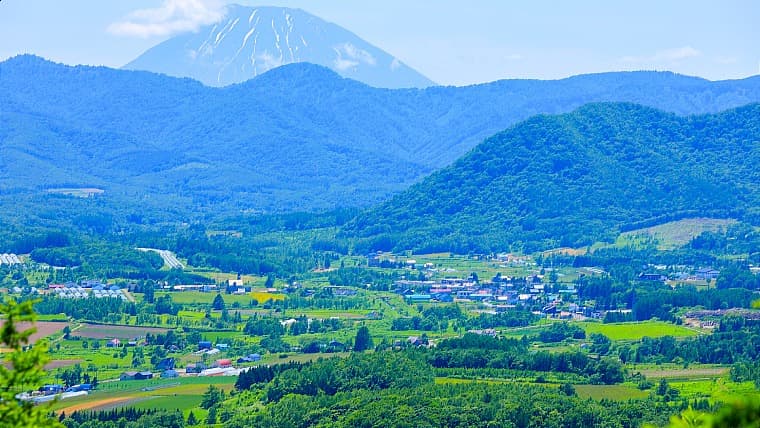 北海道赤井川村の盆地風景：カルデラ状の盆地に広がるのどかな農村地帯で、周囲の山々と美しいパッチワーク状の畑が織りなす絶景が特徴です。